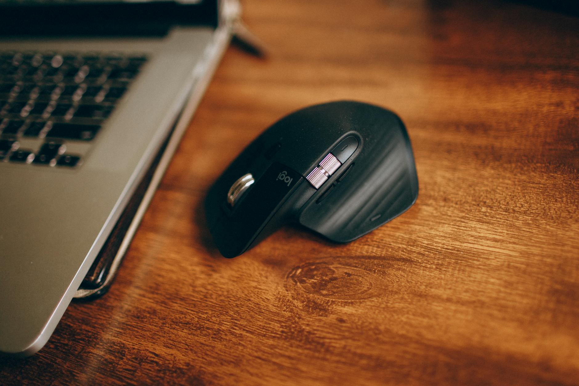 Bezprzewodowa mysz ergonomiczna obok laptopa na drewnianym biurku