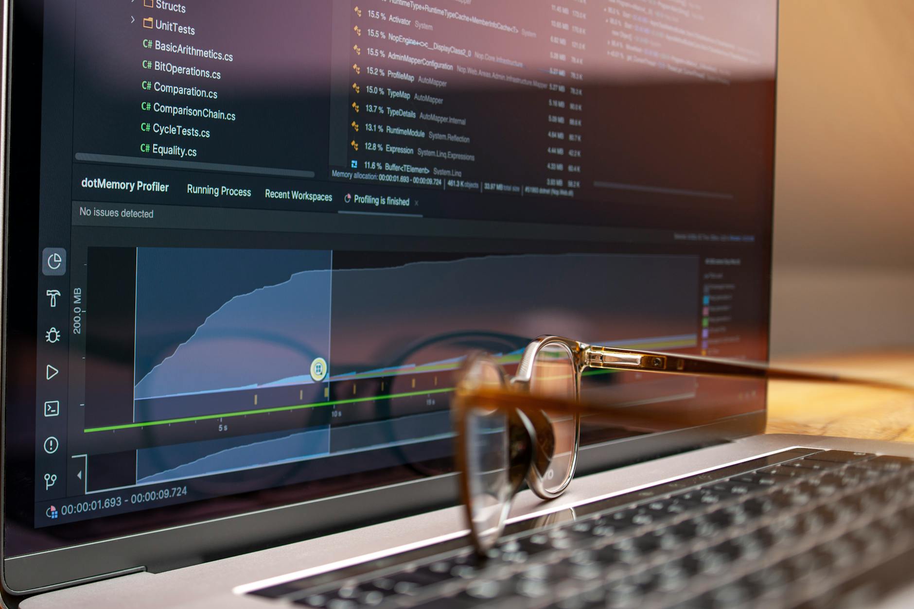 Laptop z wyświetlonym kodem i wykresami wydajności, okulary na klawiaturze